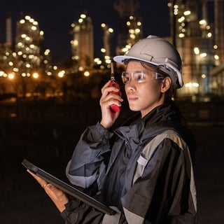 Woman with a hardhat talking into a walkie talkie holding a tablet